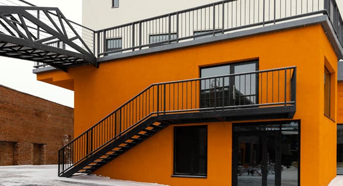 Barandales modernos de herrería color negro instalados en el balcón y la escalera exterior de una construcción de color anaranjado y blanco