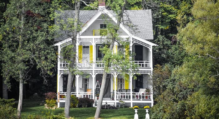 Casa antigua y grande con barandales blancos en el porche y pasillo con vista a entorno con vegetación abundante