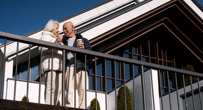 Pareja de ancianos tomando un café detrás de barandales modernos de herrería en la terraza de una casa