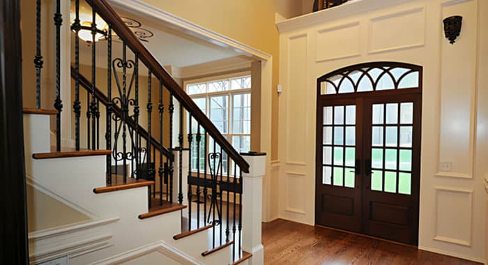 Residencia con escalera de concreto blanca con escalones revestidos con madera y un barandal con barrotes y adornos de acero