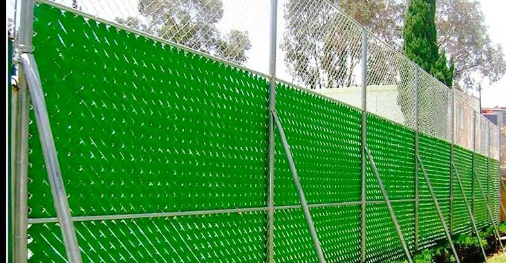 Reja de acero siendo equipada con cinta rompevientos y coronada con alambre de púas o concertina para mayor seguridad de una casa