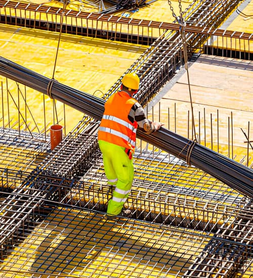 Trabajador de la construcción guiando un paquete de varillas sobre estructuras hechas con aceros de refuerzo