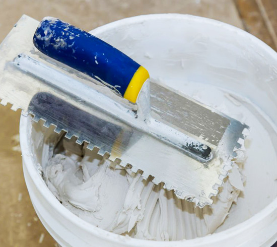 Bote lleno de mezcla de cemento blanco junto a una llana dentada