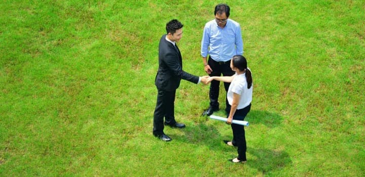 Personas de negocios estrechando las manos en medio de un terreno en venta