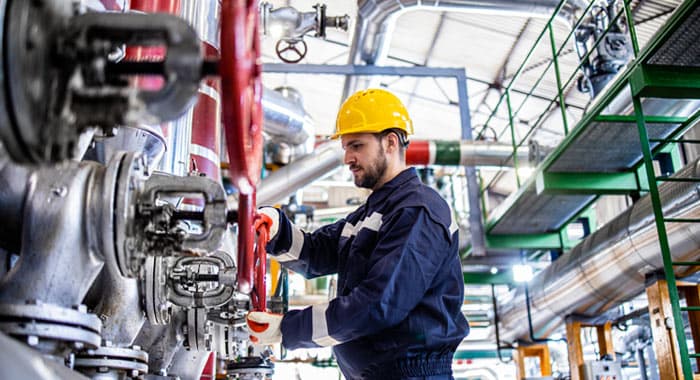 Trabajador con uniforme y casco operando equipo de refinería - Mantenimiento industrial