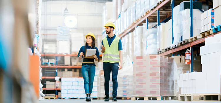 Mujer y hombre caminando entre grandes estantes industriales con diversas mercancías