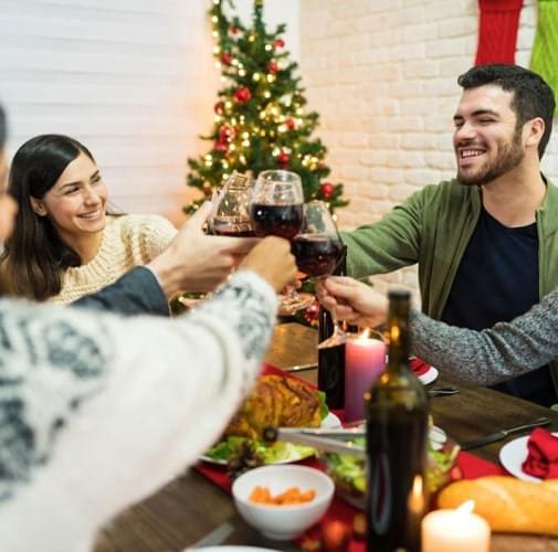 Amigos reunidos dentro de una casa brindando frente al árbol de Navidad
