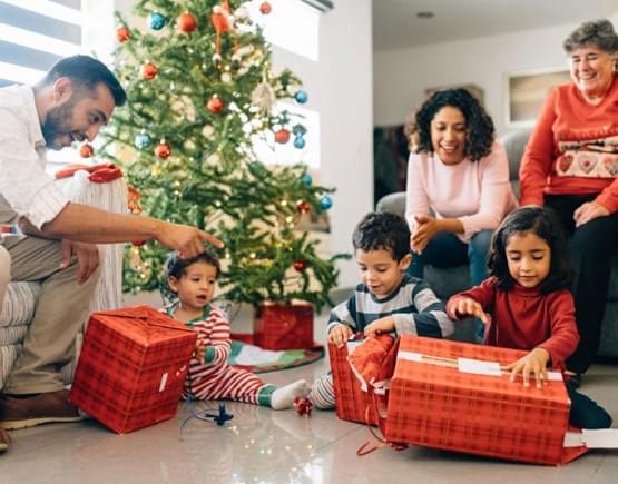 Niños sonriendo abriendo sus regalos de Navidad en compañía de sus padres