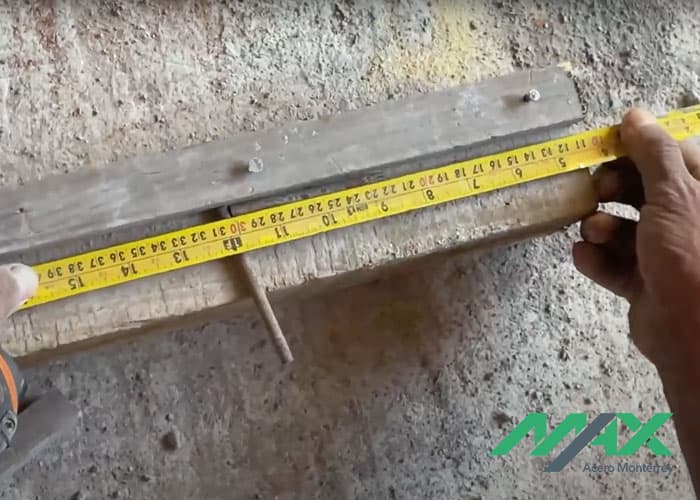 Manos midiendo con flexómetro y un tramo de alambrón en estructura para hacer estribos