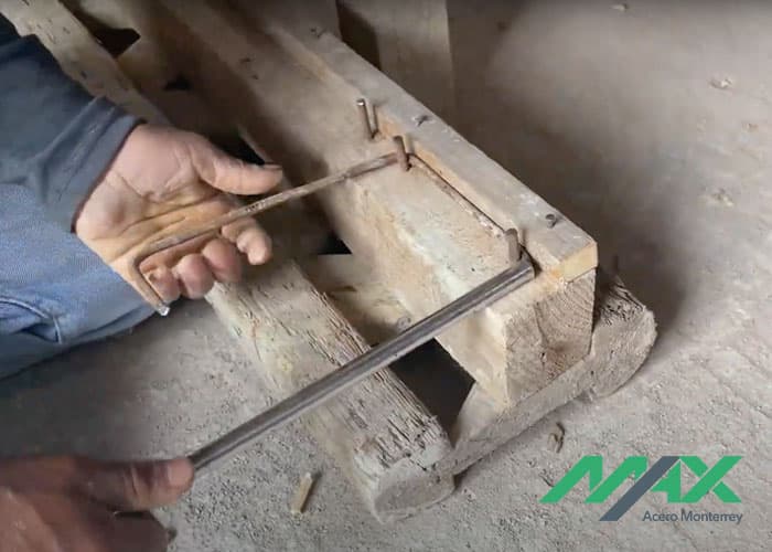 Trabajador doblando tramo de alambrón con tubo y estructura de madera para elaborar estribos