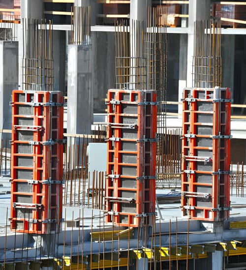 Cimbras metálicas rojas en un proyecto de construcción, sosteniendo columnas de concreto en fraguado