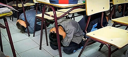 Niños debajo de su pupitre, hincados y con las manos protegiendo su cabeza