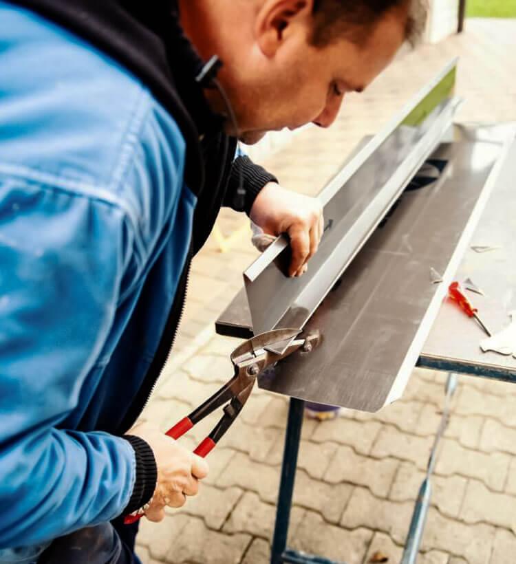 Trabajador cortando lámina utilizando un par de tijeras de hojalatero